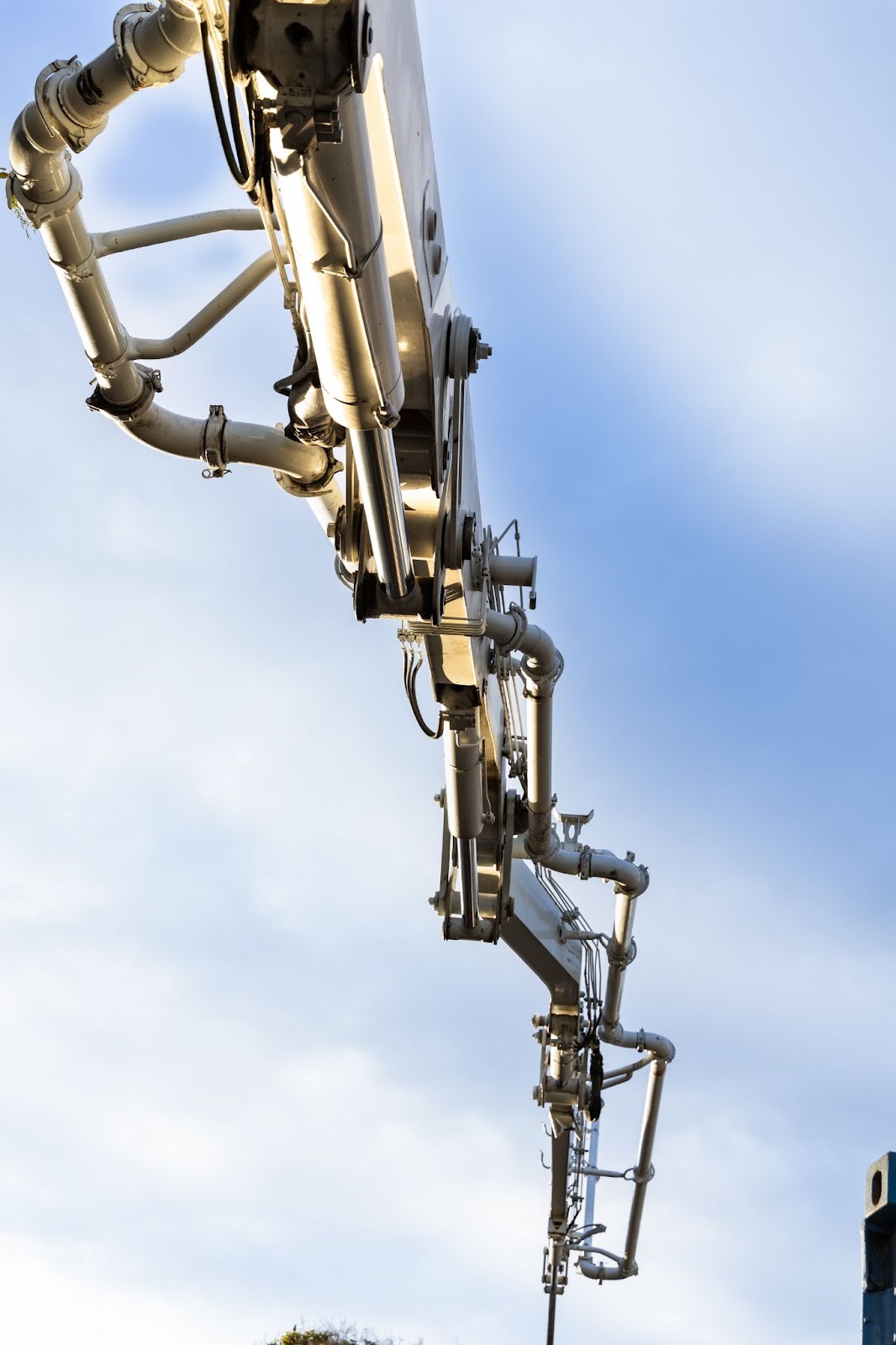 Close-up view of a concrete boom pump arm extended against the sky, showing steel joints and hydraulic components in operation.