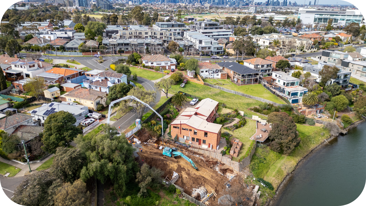 Aerial view of a suburban Melbourne neighbourhood showing a boom pump pouring concrete beside a brick building near the water.