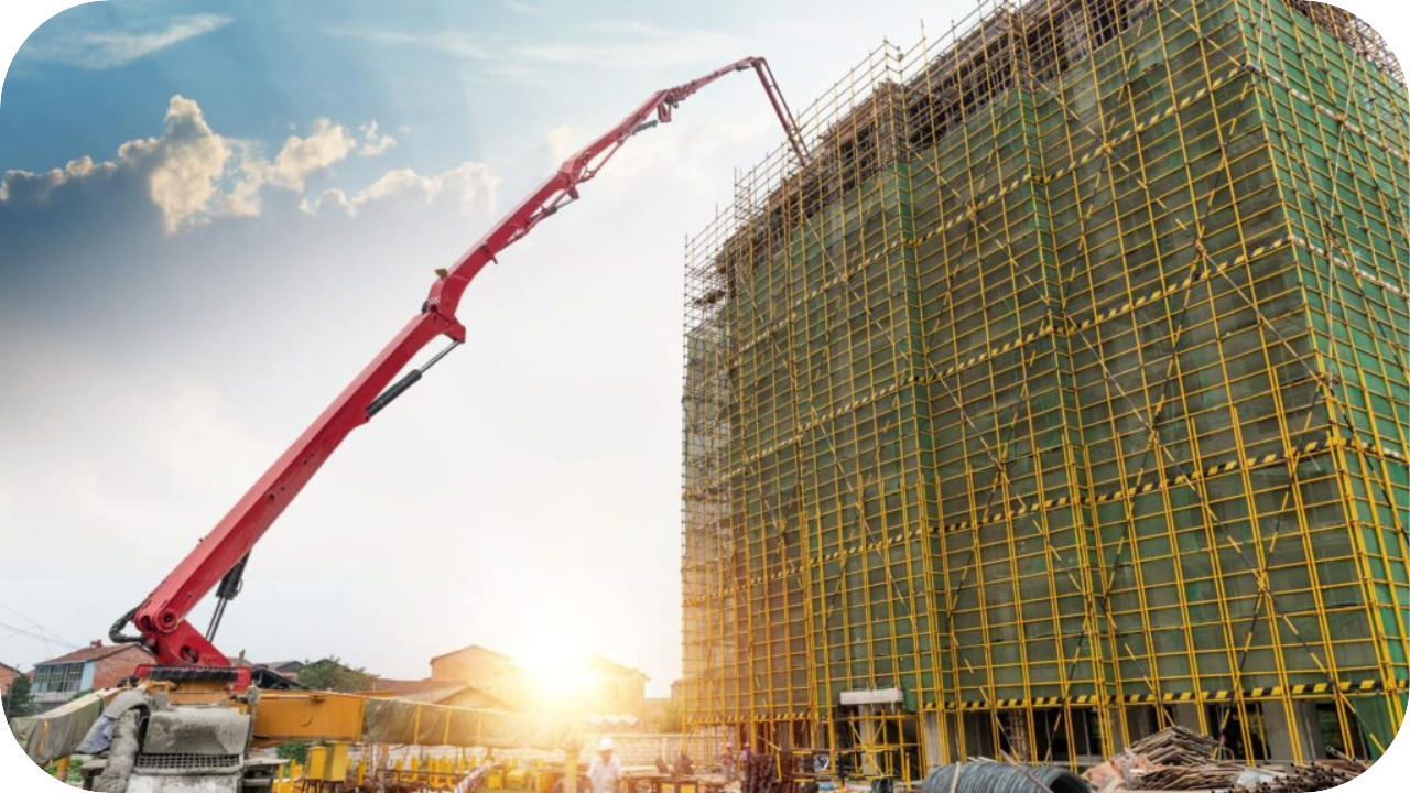 A red boom pump pours concrete onto a tall building under construction, surrounded by scaffolding and workers during sunrise.