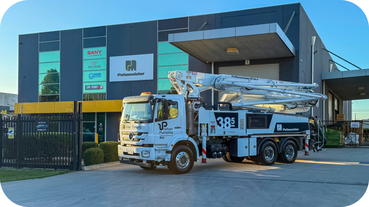A white Urban Pumping boom pump truck parked outside the Putzmeister Melbourne facility under clear blue skies.