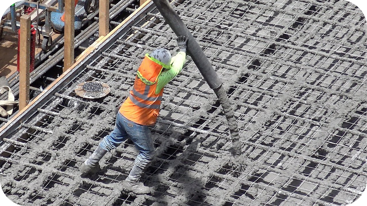 Worker in safety gear directing a concrete hose over reinforced steel mesh, demonstrating efficiency and technique in large-scale concrete pumping operations.
