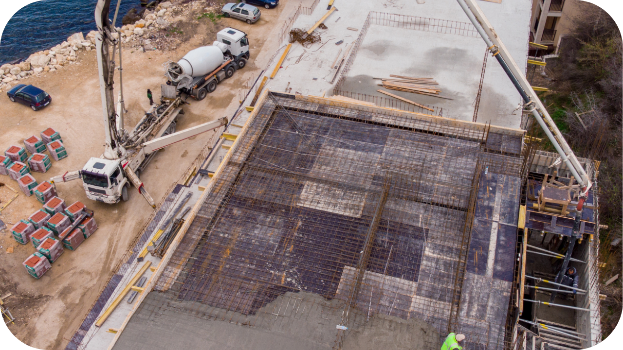Aerial view of a construction site showing concrete being pumped into a steel-reinforced floor slab with a boom pump truck in use.