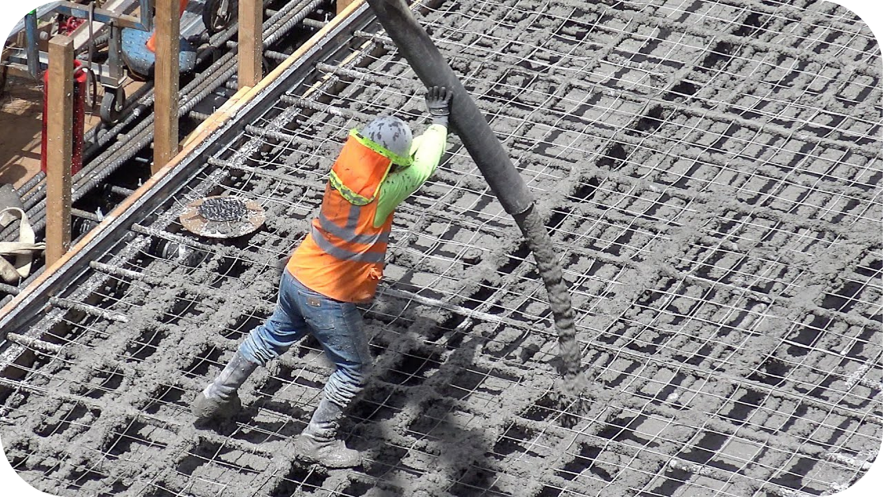 Worker placing concrete from a pump hose over reinforced steel mesh on a construction slab, showing controlled flow and efficient onsite pumping.
