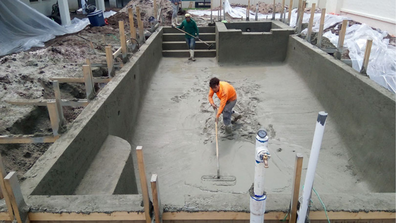 Workers are spreading and smoothing fresh concrete across a rectangular pool shell during construction, preparing an even base for a strong residential pool in Melbourne.