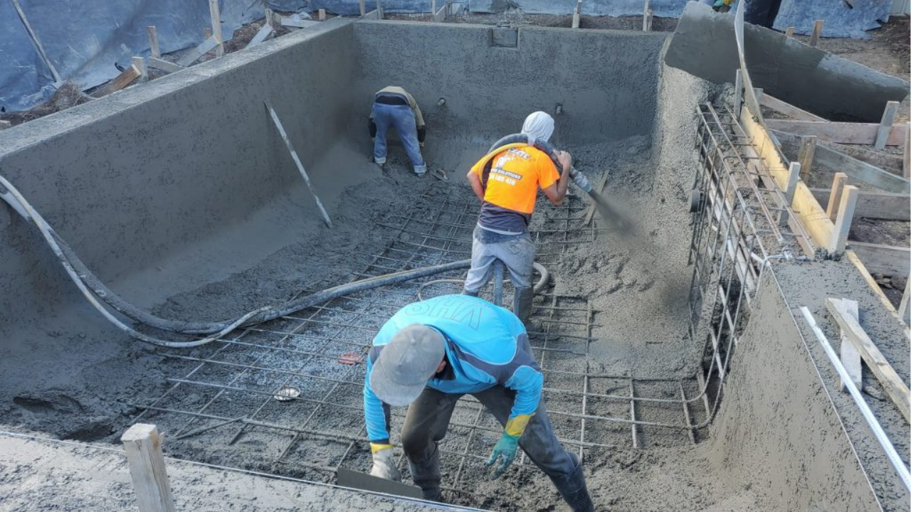 Crew pumping and smoothing fresh concrete over steel reinforcement inside a residential pool shell, shaping the structure during Melbourne pool construction.