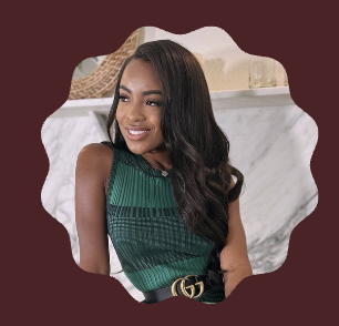 Smiling woman with long dark hair wearing a green sleeveless top and black belt seated indoors.