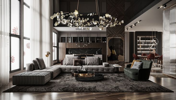 Modern living room with a large gray sectional sofa, green armchair, round coffee tables, elaborate chandelier, and open kitchen in the background.