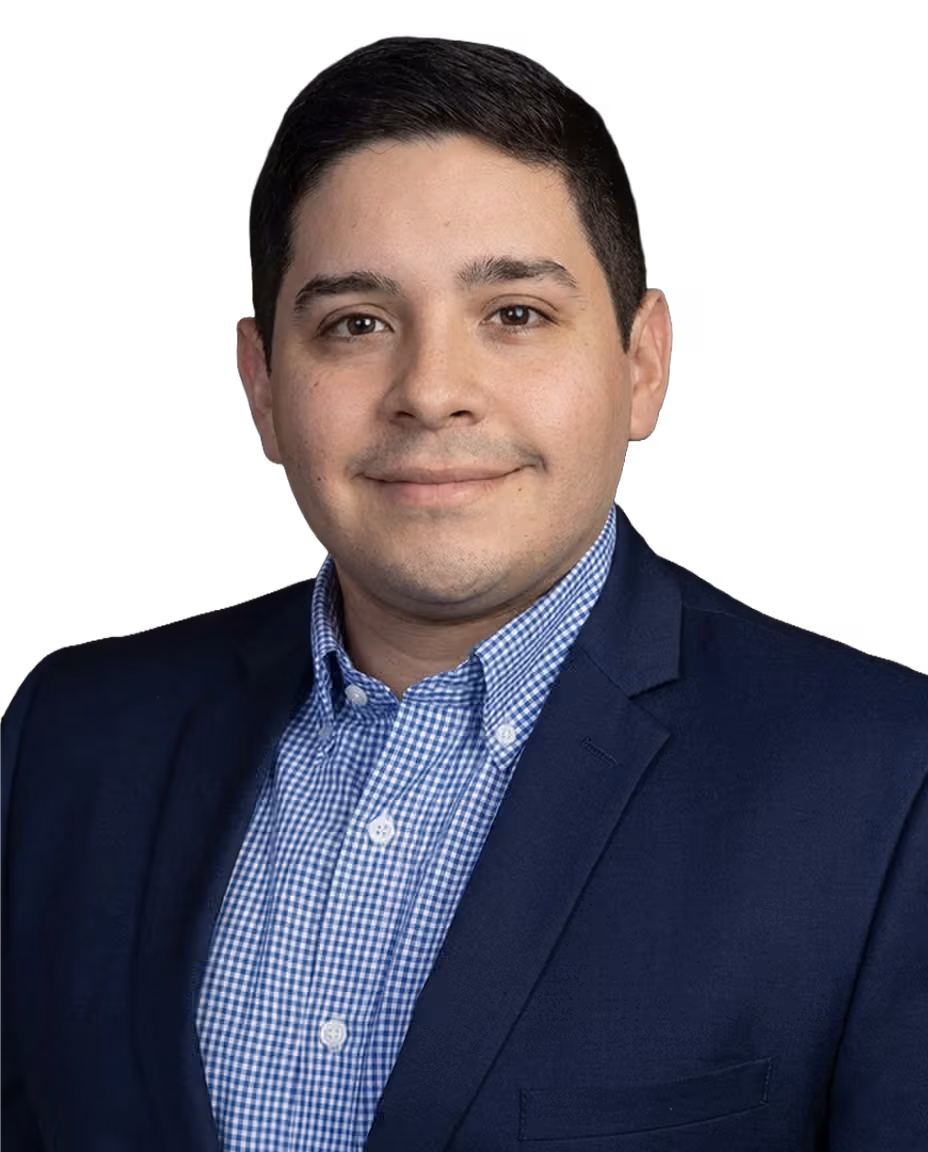 Male audiologist with short black hair wearing a blue checkered shirt and navy blazer against a black background.