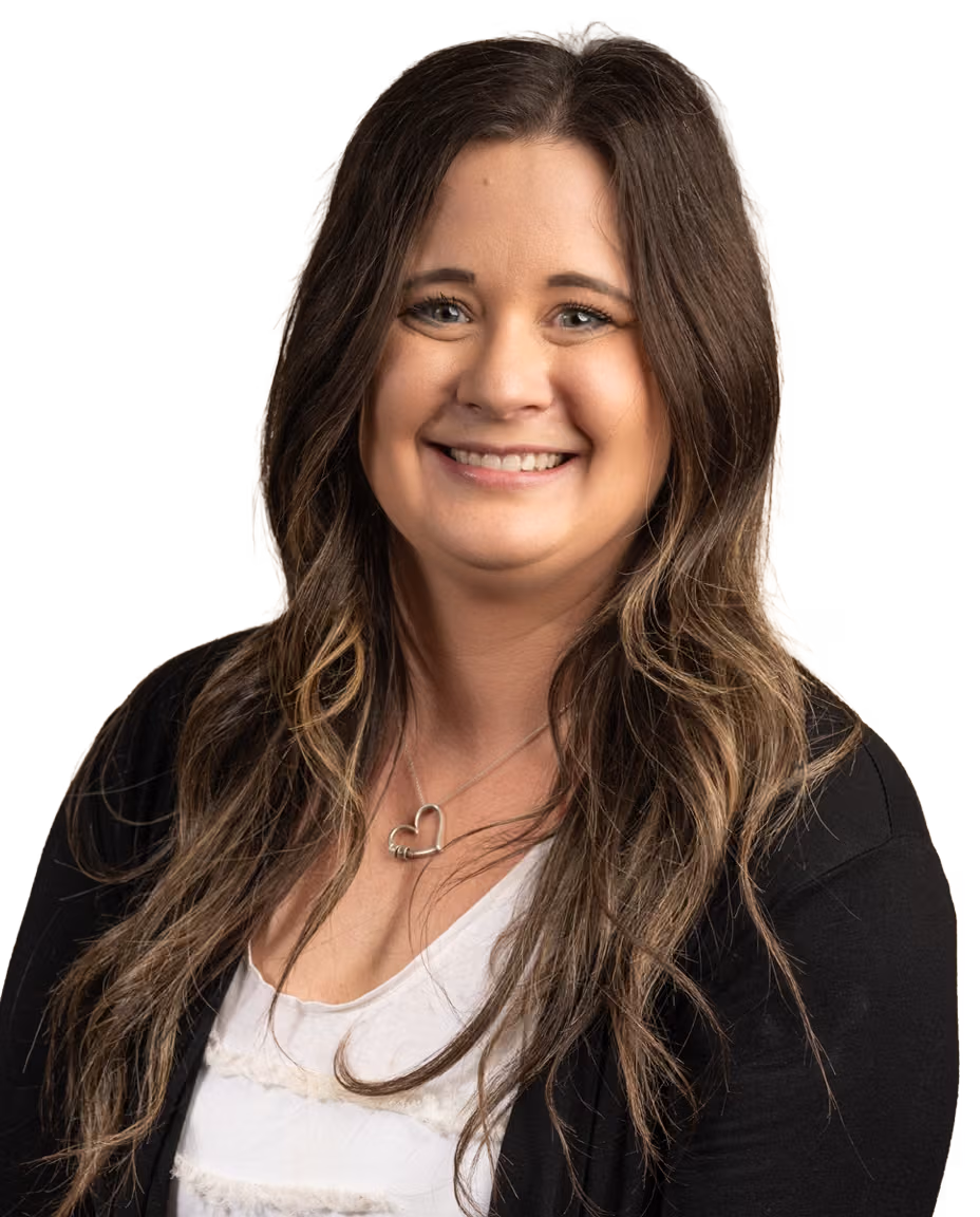Smiling female audiologist with long brown hair wearing a white top, black cardigan, and heart-shaped necklace.