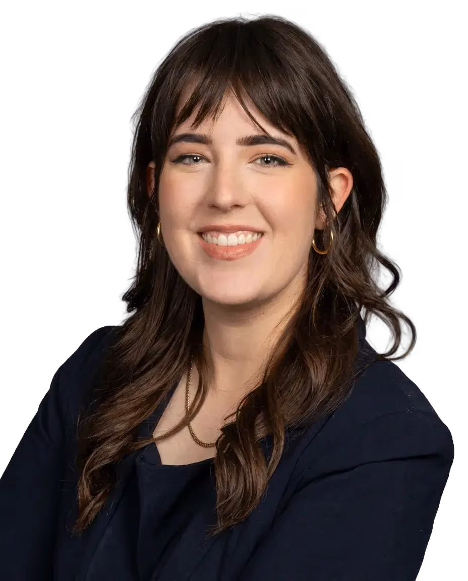 Smiling female audiologist with long brown hair, wearing a dark blazer and gold hoop earrings.