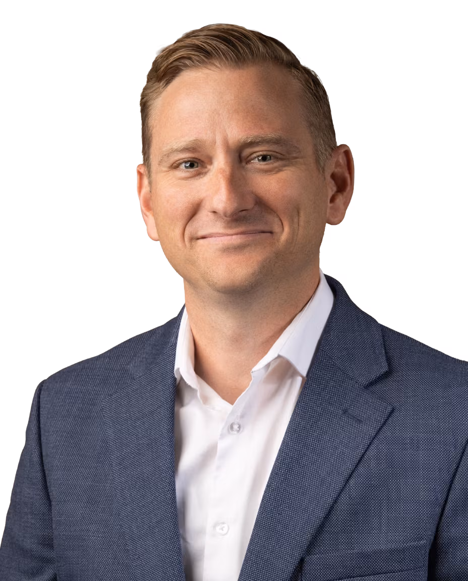 Smiling male audiologist with short light brown hair wearing a blue blazer and white shirt against a white background.