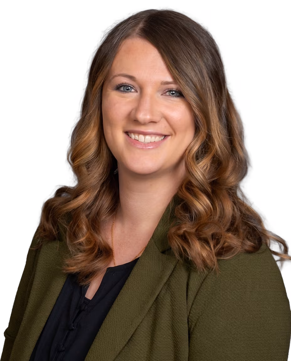 Portrait of a smiling female audiologist with long curly brown hair wearing a green blazer and black top.