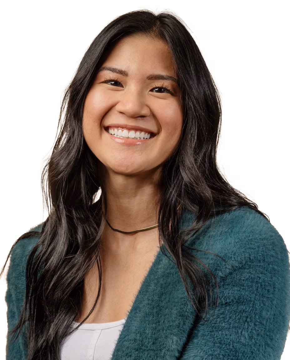 Smiling female audiologist with long dark hair wearing a teal fuzzy sweater and gold necklace.