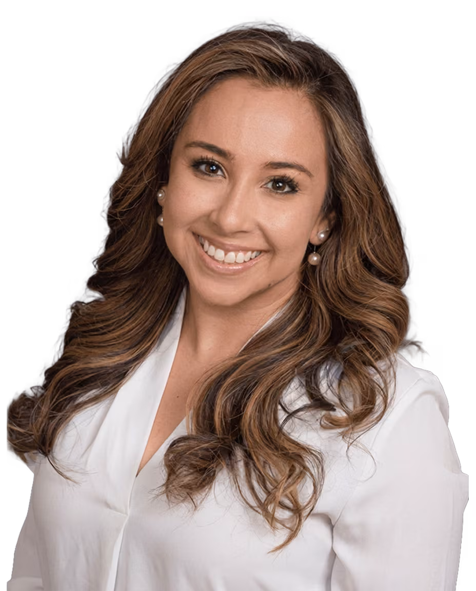 Smiling female audiologist with long wavy brown hair wearing pearl earrings and a white blouse.
