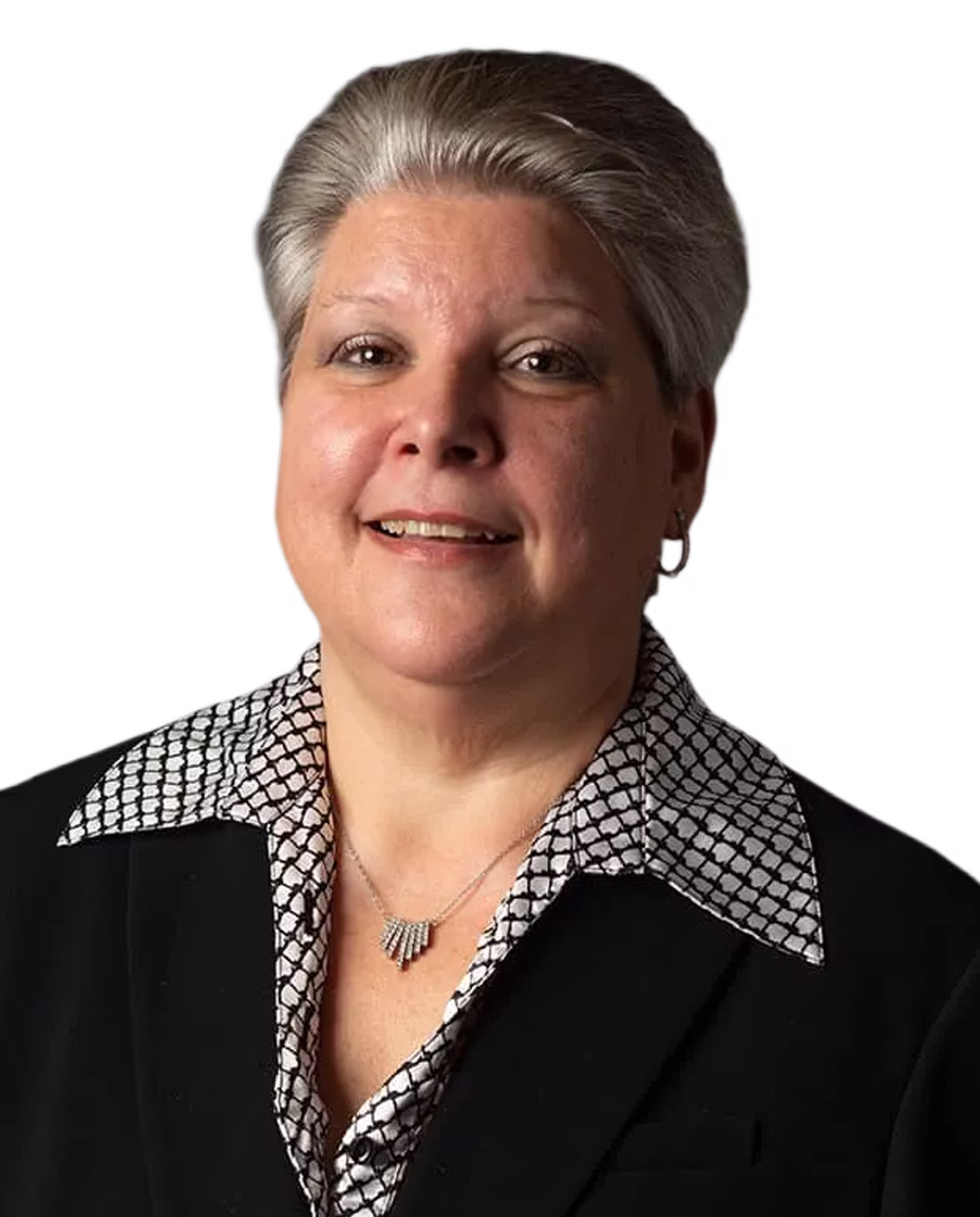 Smiling female hearing specialist with short gray hair wearing a black blazer over a patterned white shirt and a silver necklace.