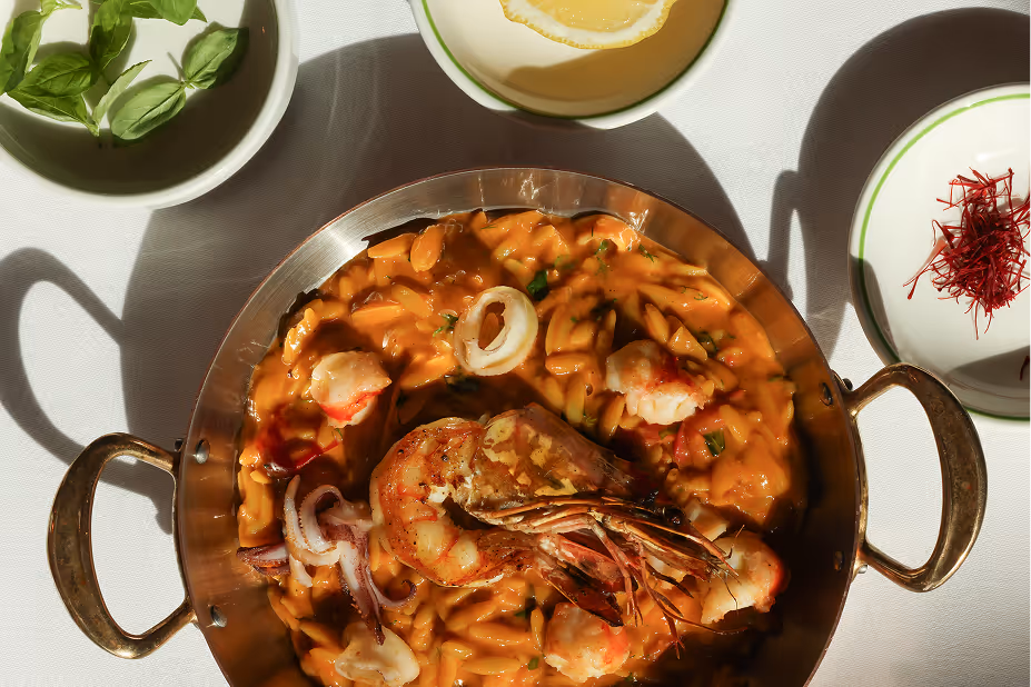 A pan filled with pasta and shrimp on top of a table in Novikov Abu Dhabi restuarant