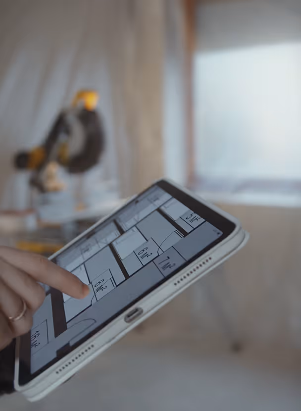 Person holding a tablet displaying a floor plan with room measurements.