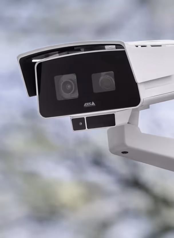 Close-up of a white Axis security surveillance camera mounted outdoors with a blurred natural background.