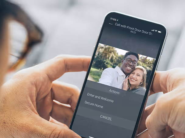 Person holding a smartphone displaying a video call with a smiling couple and options to enter and welcome or secure home.