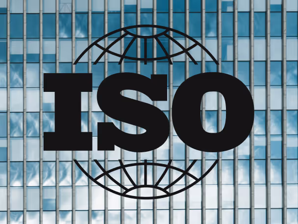 Black ISO letters over a globe icon in front of a glass building facade with reflected sky and clouds.