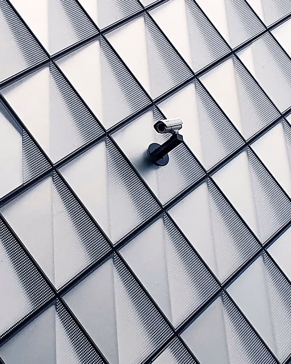 Security camera mounted on a geometric patterned glass building facade.