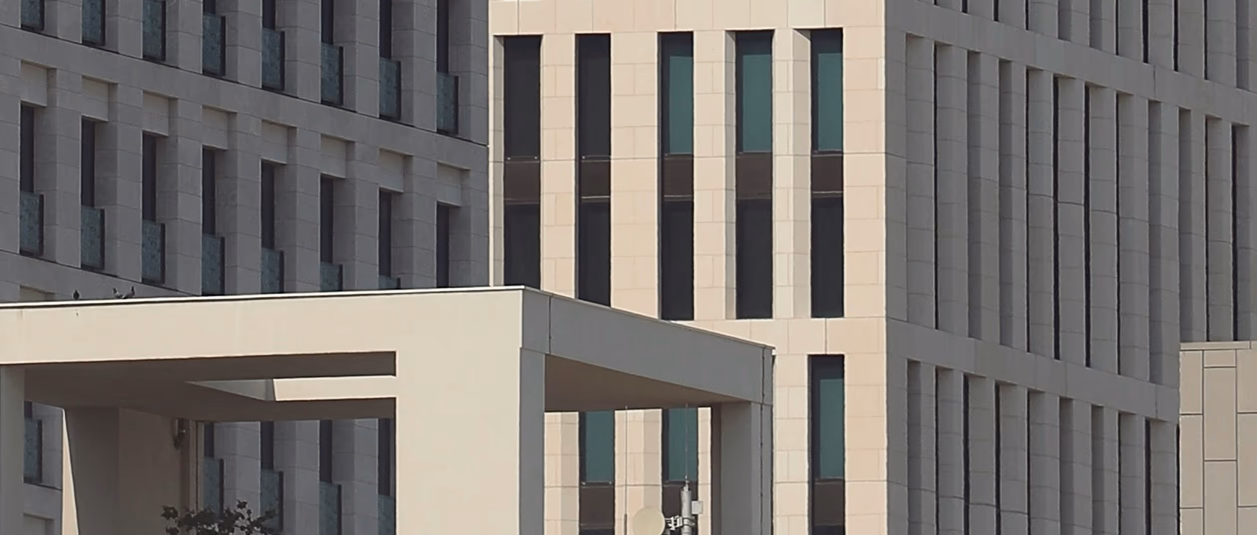 Modern office building facade with vertical windows and a beige architectural structure in the foreground.