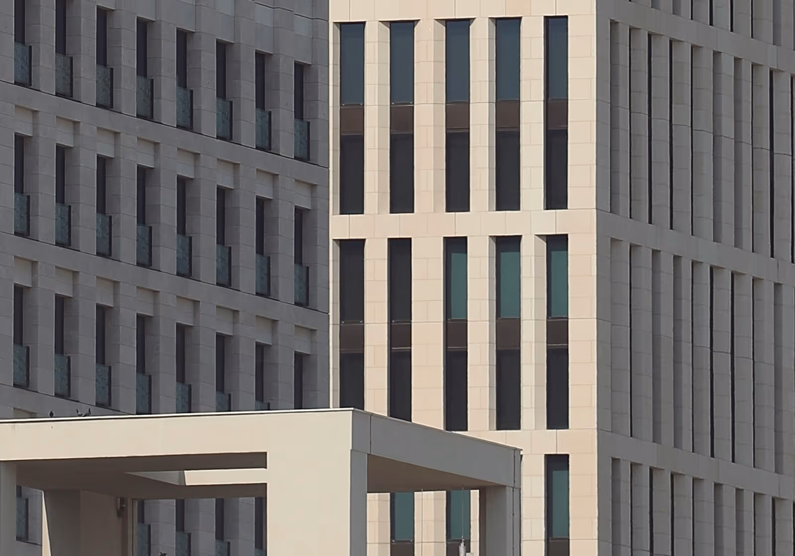Modern high-rise buildings with a grid-like pattern of windows and a white canopy structure in the foreground.