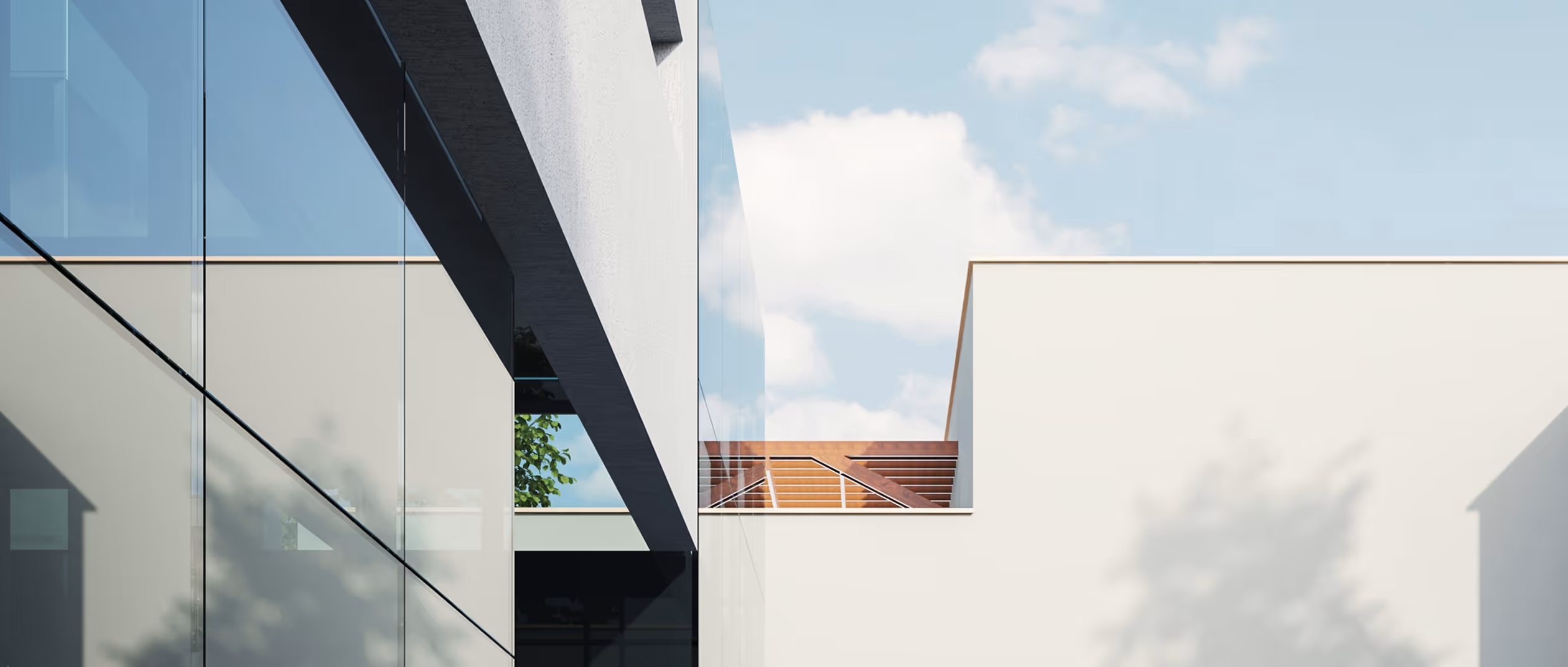 Modern building exterior with large glass windows reflecting the sky and a rooftop terrace with wooden railing under a cloudy blue sky.