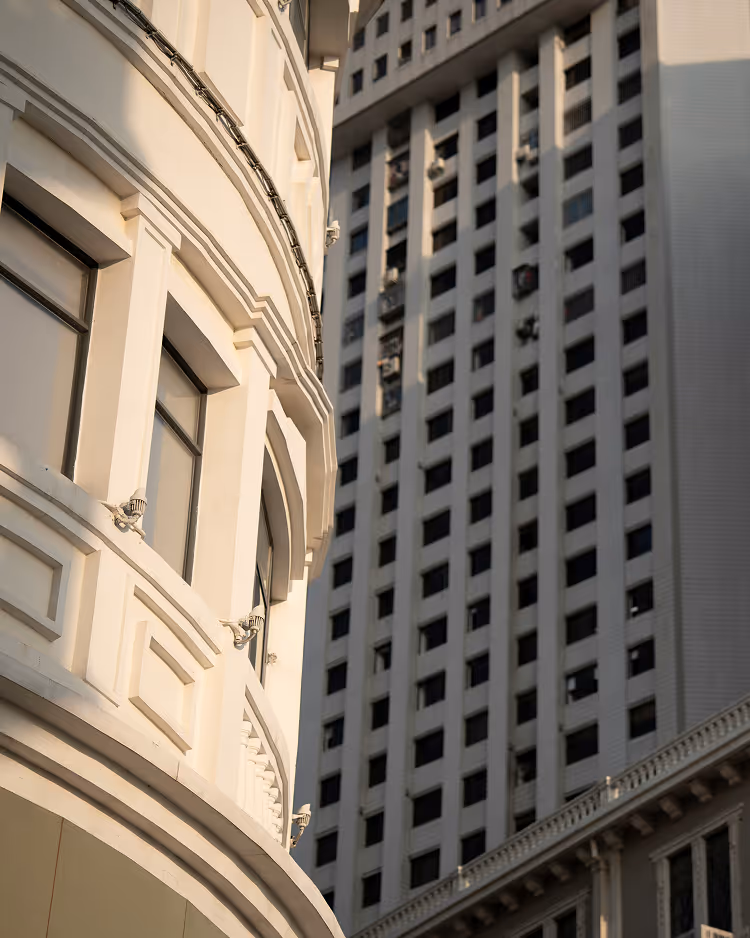 Close-up of a white curved building facade with windows and decorative moldings next to a tall modern building with a grid of windows.