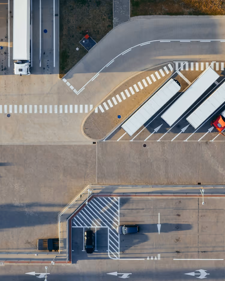 Aerial view of a parking lot with several parked trucks and cars, marked lanes, and pedestrian crosswalks.