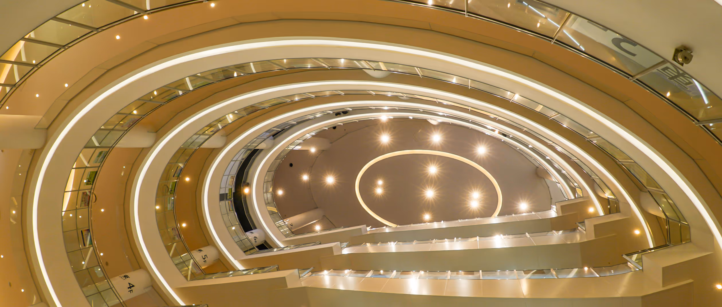 Interior view looking up at the curved multiple floors with illuminated railings and ceiling lights in a modern building.