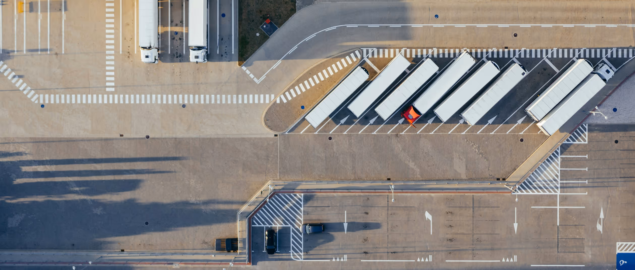 Aerial view of a parking area with six white trucks parked diagonally and a single red truck among them.