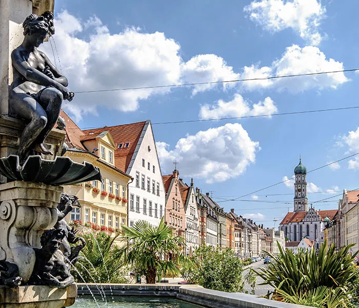 Eine idyllische Straßenszene mit einem Brunnen im Vordergrund und historischen Häusern in Bayern.