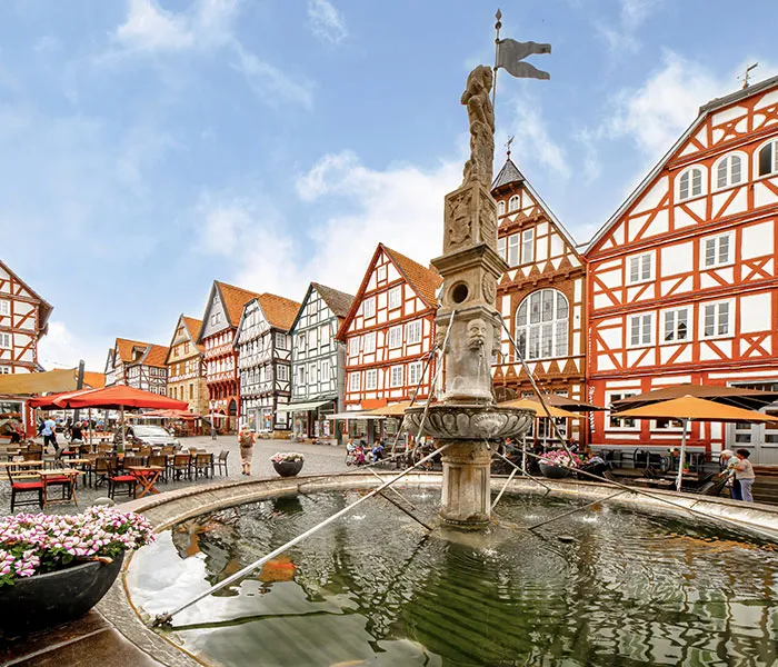 Ein Brunnen vor roten Fachwerkhäusern in Hessen.
