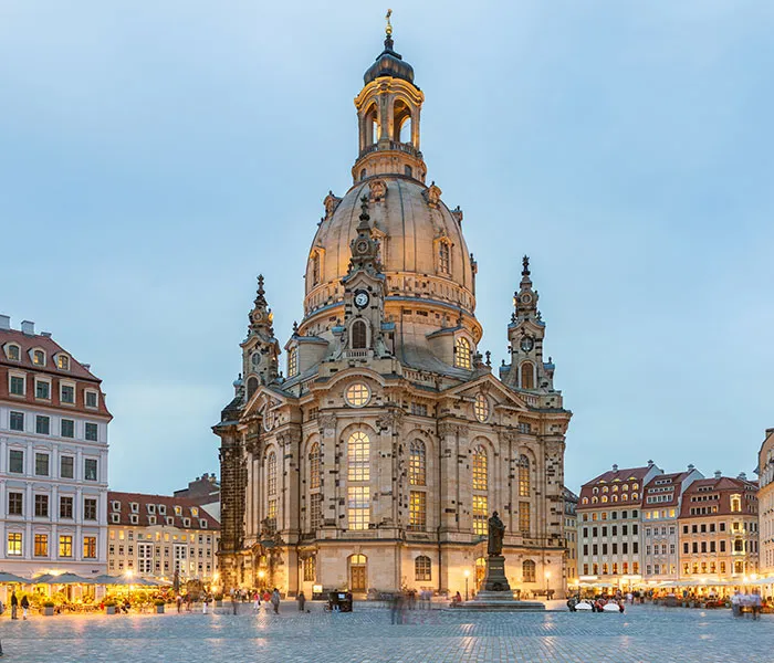Barocker Platz in Sachsen mit einer beleuchteten Kirche und umliegenden historischen Gebäuden bei Abendstimmung.