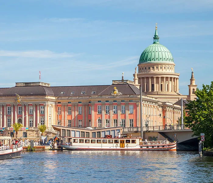 Potsdamer Stadtschloss am Ufer eines Flusses, vor blauem Himmel.