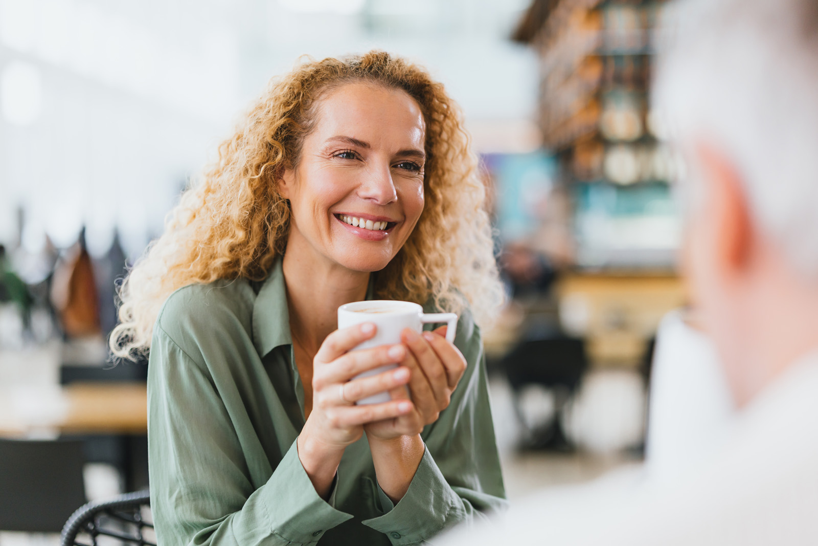 Markenfotografie: Frau mit Kaffeebecher lächelt in einem Café am Flughafen München
