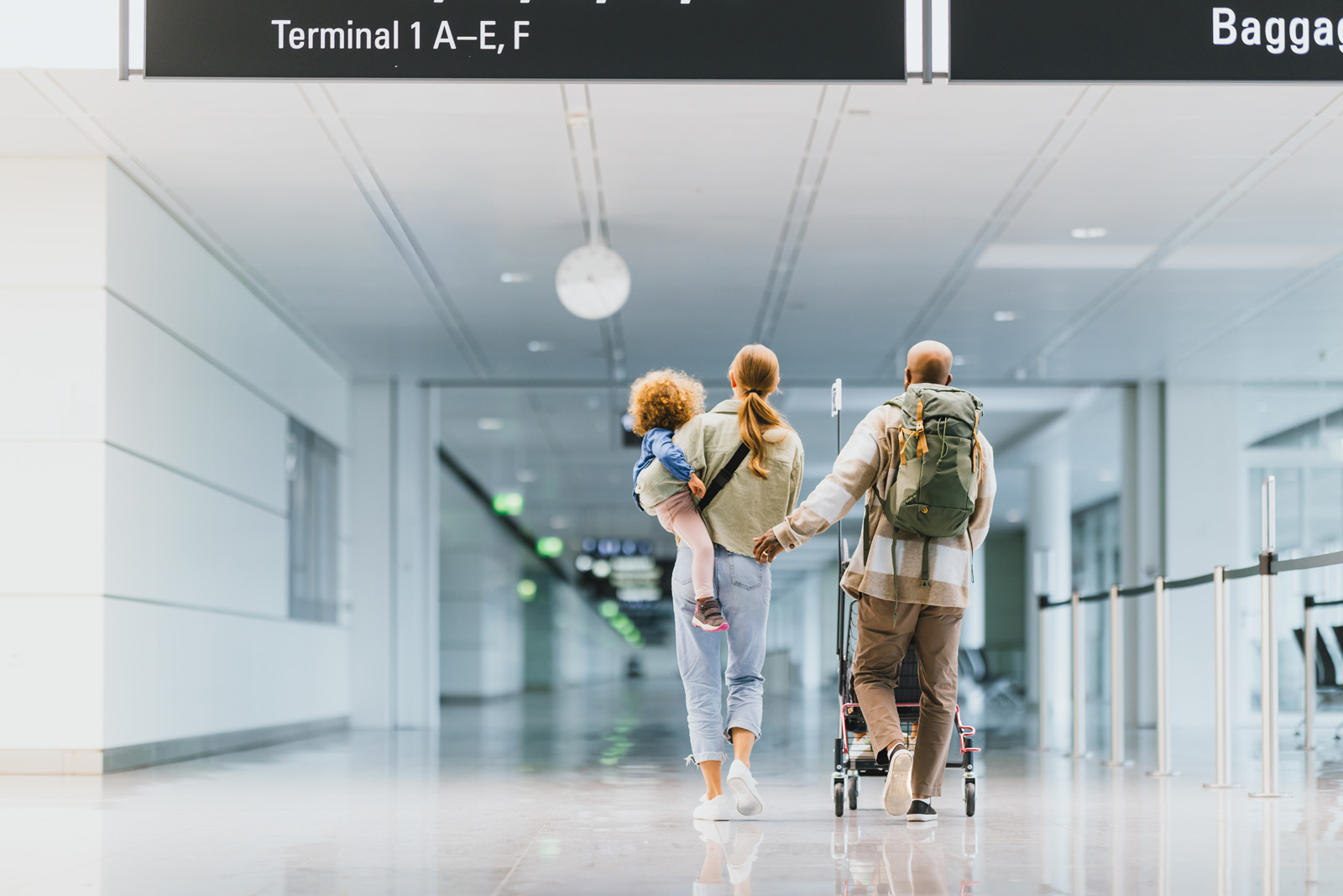 Markenfotografie: Familie läuft durch das Terminal des Flughafens München, im Hintergrund die Wegweiser