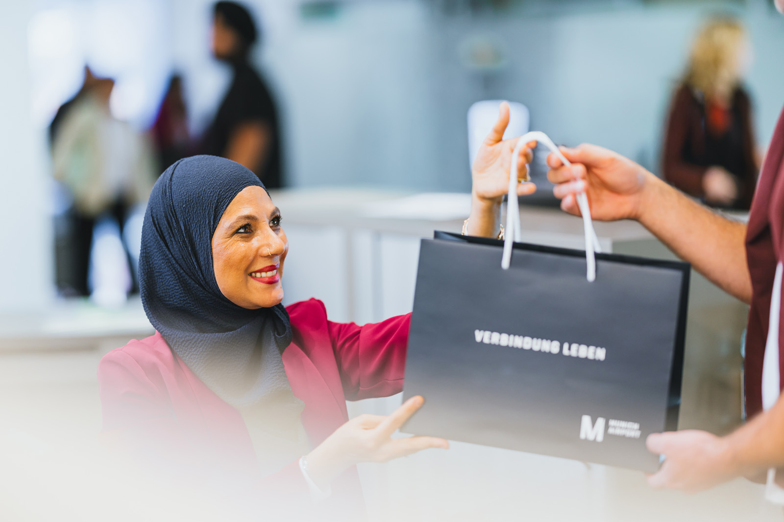 Markenfotografie: Verkäuferin übergibt eine schwarze Einkaufstasche in einem Shop am Flughafen München
