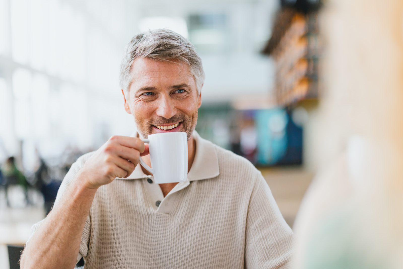 Markenfotografie: Mann mit Kaffeetasse lächelt in einem Café am Flughafen München
