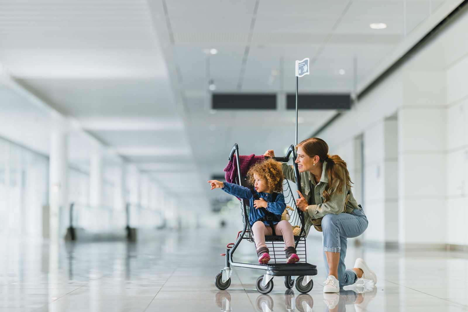 Markenfotografie: Vater schiebt sein Kind in einem Gepäckwagen durch das Terminal des Flughafens München