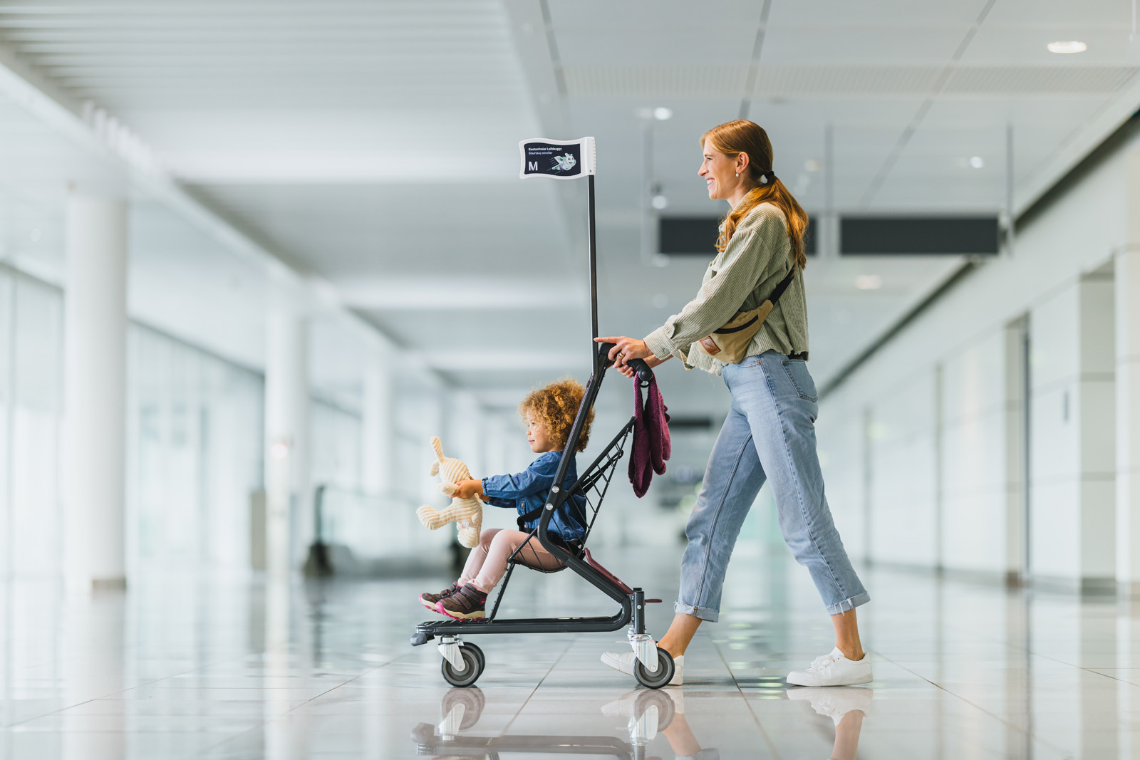 Markenfotografie: Mutter schiebt ihr Kind im Kinderwagen durch das helle Terminal des Flughafens München