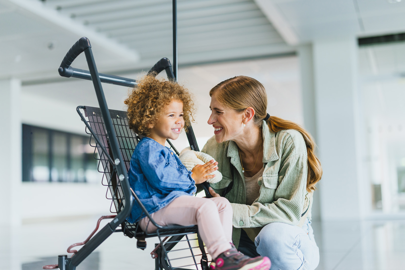 Markenfotografie: Mutter kniet neben ihrem Kind im Kinderwagen am Flughafen München