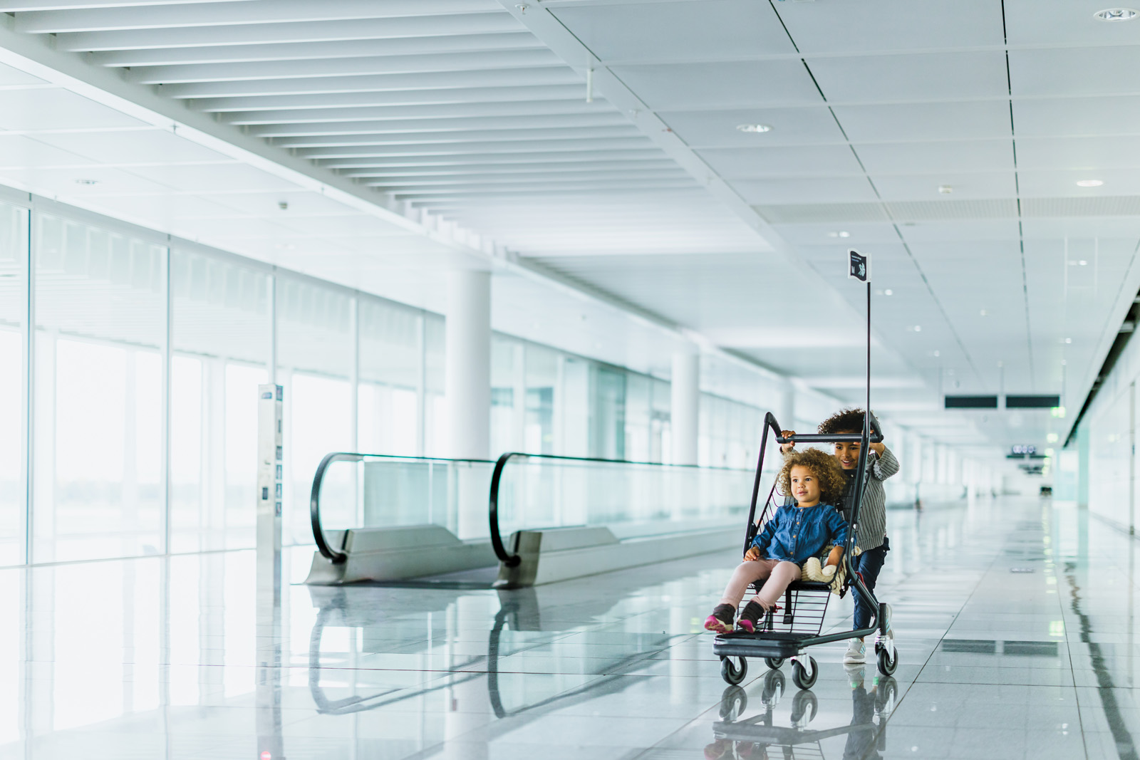Markenfotografie: Frau mit Gepäckwagen vor der Rolltreppe im Terminal des Flughafens München