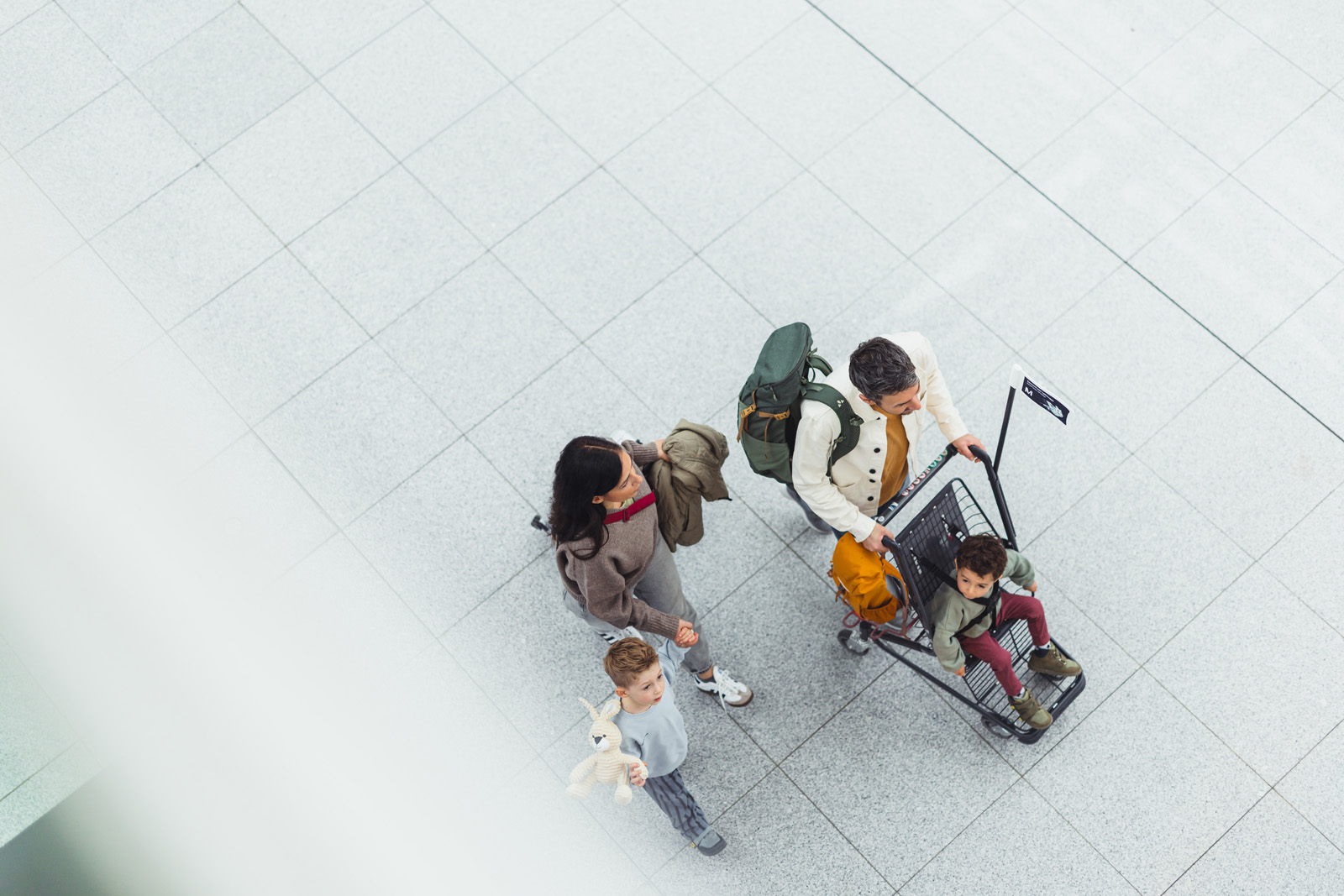 Markenfotografie: Familie mit Gepäckwagen von oben im Terminal des Flughafens München
