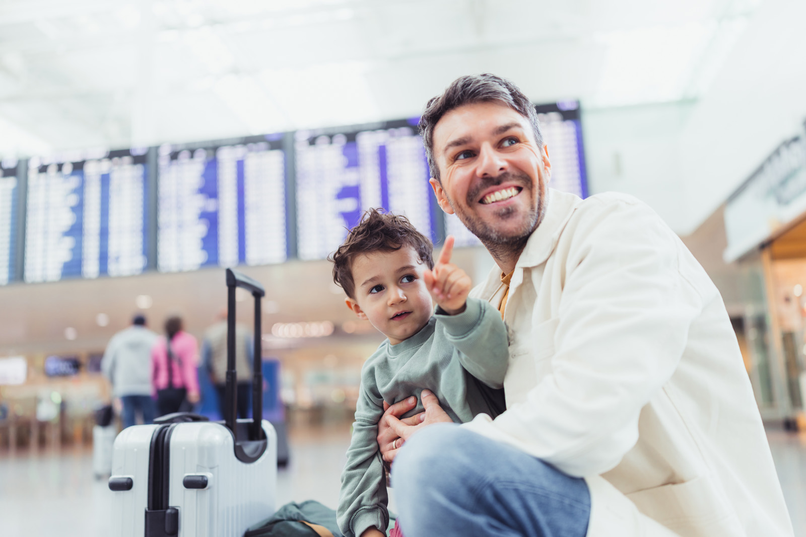 Markenfotografie: Vater mit Kind im Gepäckwagen vor der Anzeigetafel im Terminal des Flughafens München