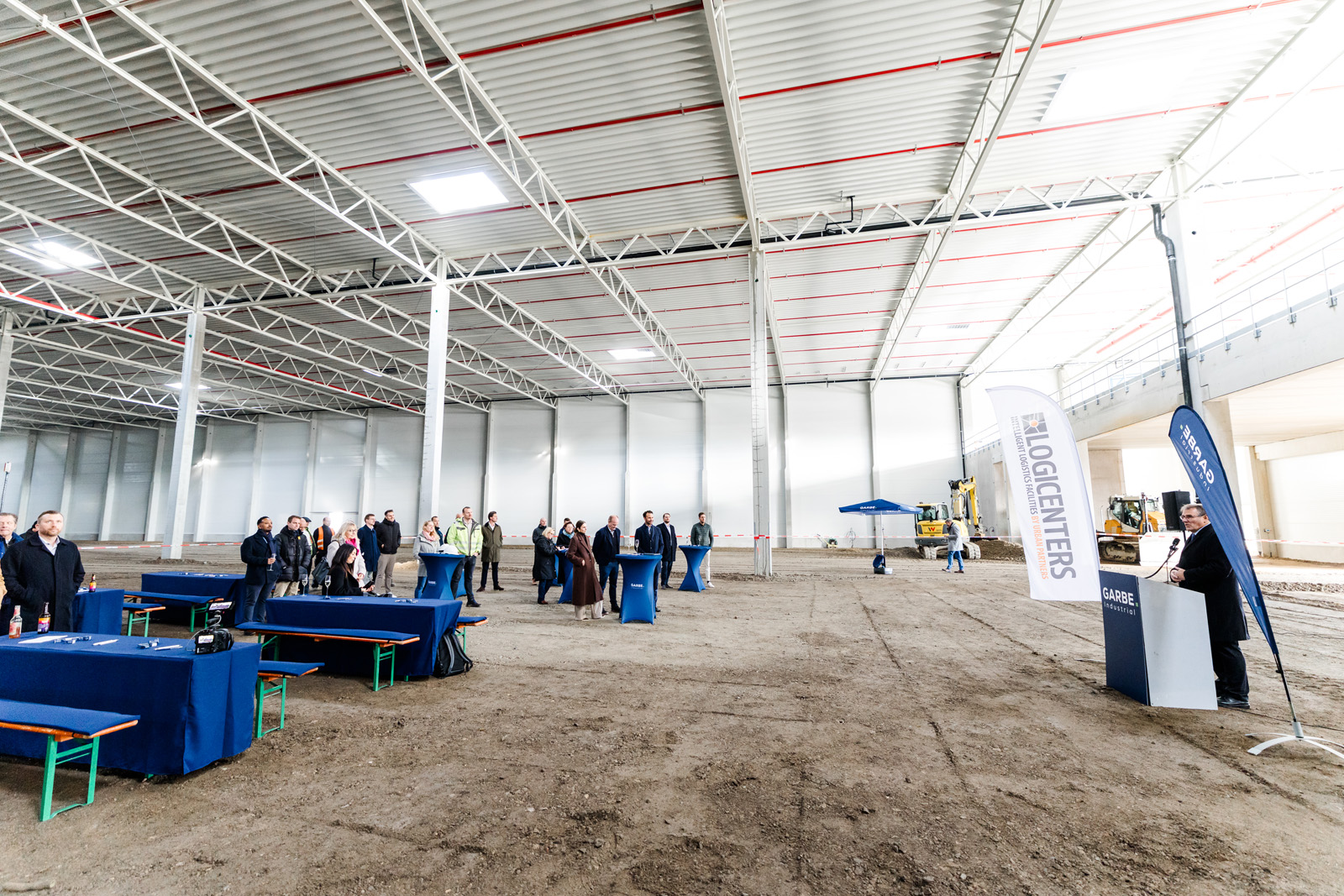 Eventfotografie: Weite Halle im Rohbau mit Baumaschinen beim Richtfest der GARBE Logistikhalle in Leipheim