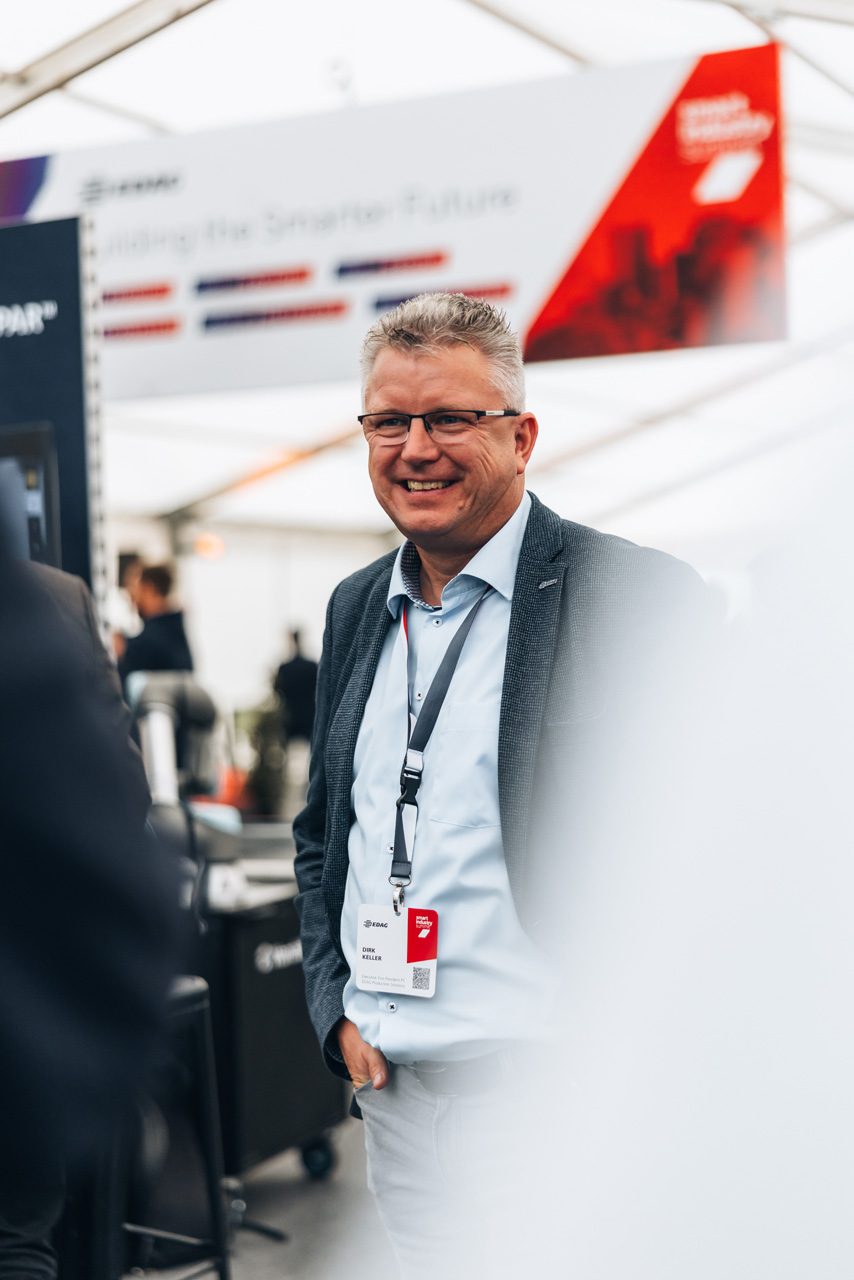 Eventfotografie: Mann mit Brille und Namensschild lächelt beim EDAG Smart Industry Summit 2025 in Fulda