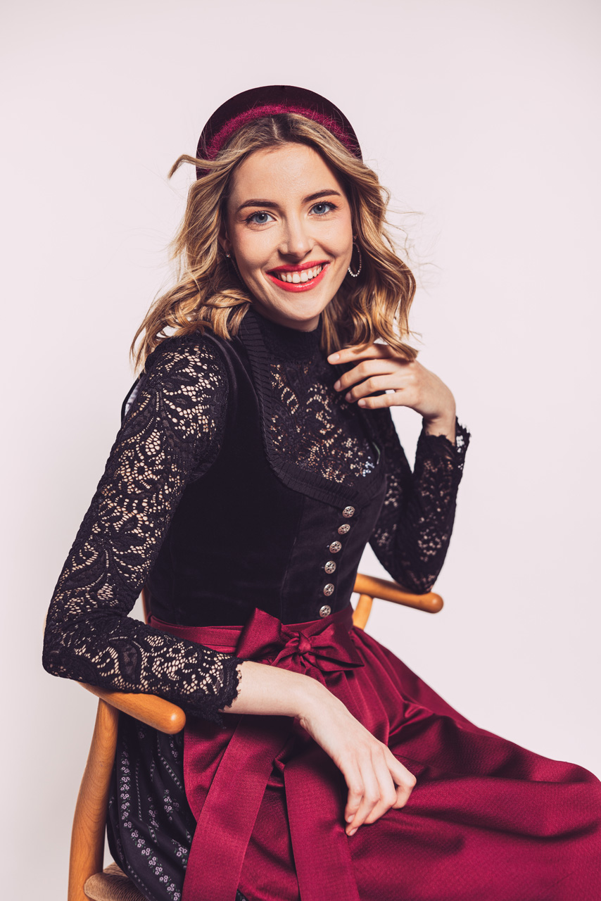 Modefotografie: Junge lachende Frau in einem dunkeln Dirndl mit roter Schürze von Silk&Pearls