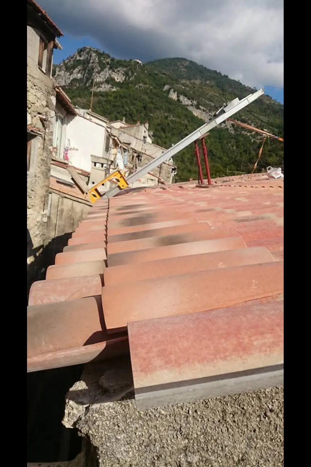 Toiture en tuiles rouges en cours de rénovation dans un village de montagne, avec échelle et vue sur les sommets.
